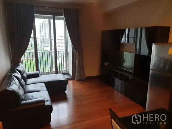 公寓 出租在Khlong Toei, Bangkok - 客厅配L型黑色皮沙发与电视柜，连通阳台赏城市景观