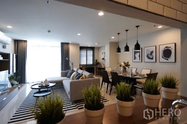 公寓 出租在Watthana, Bangkok - 开放式客餐厅，灰色沙发、条纹地毯、吊灯与布置好的餐桌。