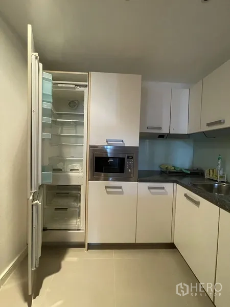Condominium for rent or sale in Watthana, Bangkok - Kitchen with integrated fridge open to show storage, plus built-in microwave and sleek white cabinets.