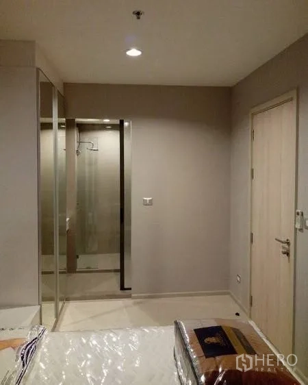 Condominium for rent in Khlong Toei, Bangkok - Bedroom corner with mirrored wardrobe and doorway to a glass-enclosed shower bathroom under warm lighting.