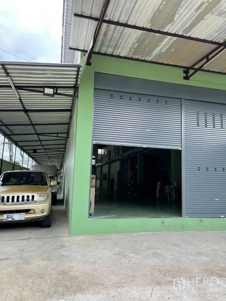 Warehouse for rent in Khan Na Yao, Bangkok - Covered loading bay with large roller shutter and carport for deliveries.