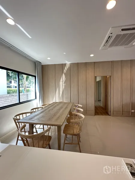 Detached House for sale in Lam Luk Ka, Pathum Thani - Dining room with six-seat wooden table beside a large window and wood panel walls.