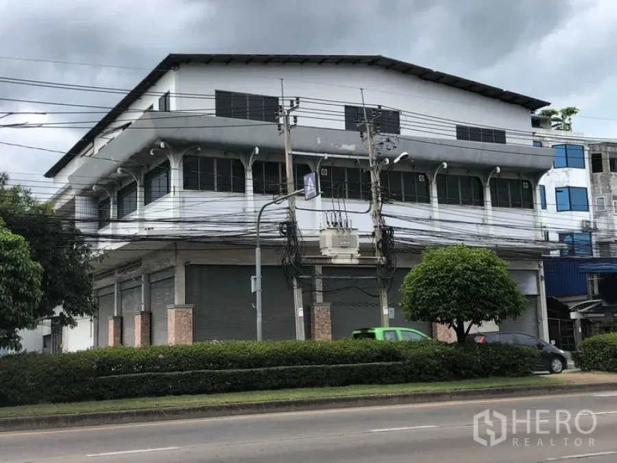 Home Office for rent in Khan Na Yao, Bangkok - Corner view of the home office building with long rows of upper-floor windows facing the main road with greenery and traffic lanes.