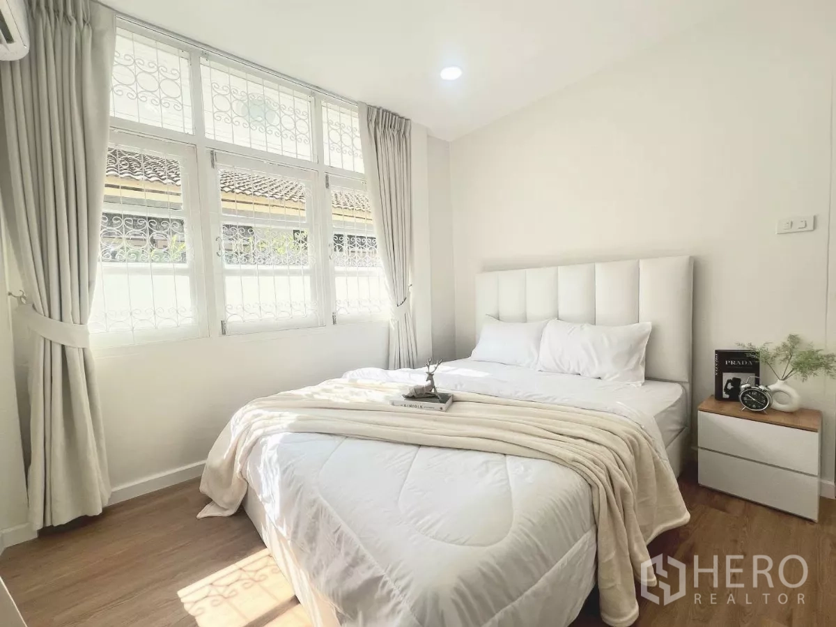 Detached House for rent in Huai Khwang, Bangkok - Guest bedroom with padded headboard, white bedding and large windows.