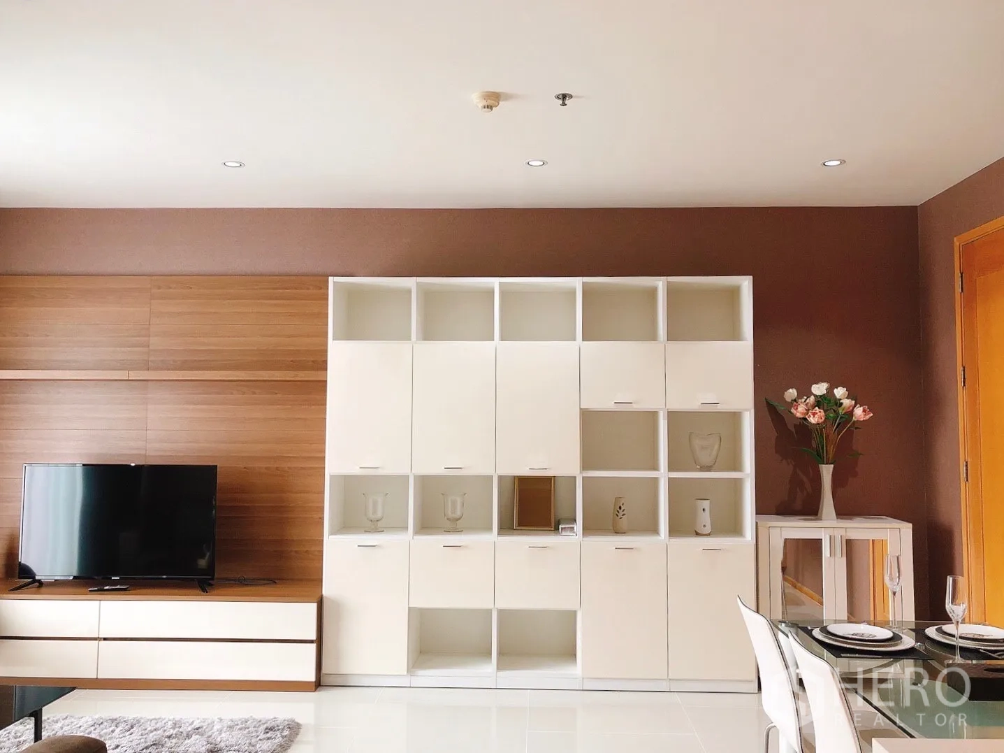 Condominium for rent in Khlong Toei, Bangkok - Built-in shelving beside the TV console and a dining area in an open-plan space.