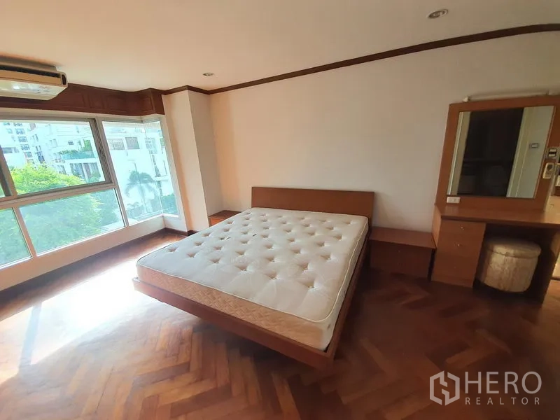 Condominium for rent in Pathum Wan, Bangkok - Corner bedroom with wood floors and wide windows overlooking greenery.