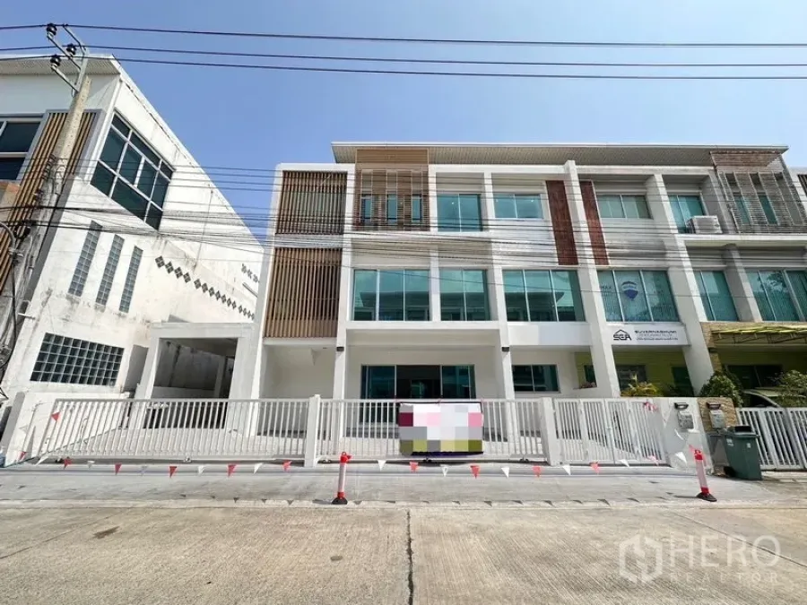Home Office for sale in Lat Krabang, Bangkok - Front view of a modern three-storey home office with large glass windows, white facade and gated driveway.