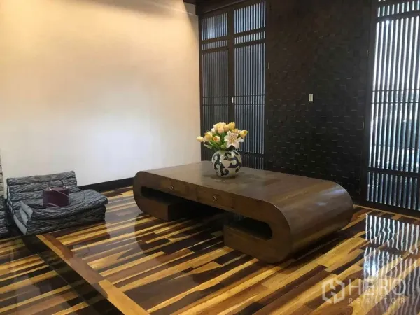 Townhouse for rent in Yan Nawa, Bangkok - Thai-inspired living area with glossy striped hardwood floors and a sculpted low wooden table.