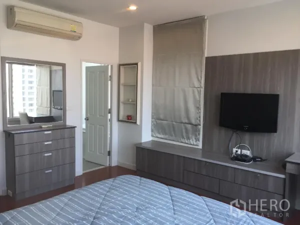 Condominium for rent or sale in Khlong Toei, Bangkok - Master bedroom with grey custom cabinetry, dresser, mounted TV, and air conditioning.