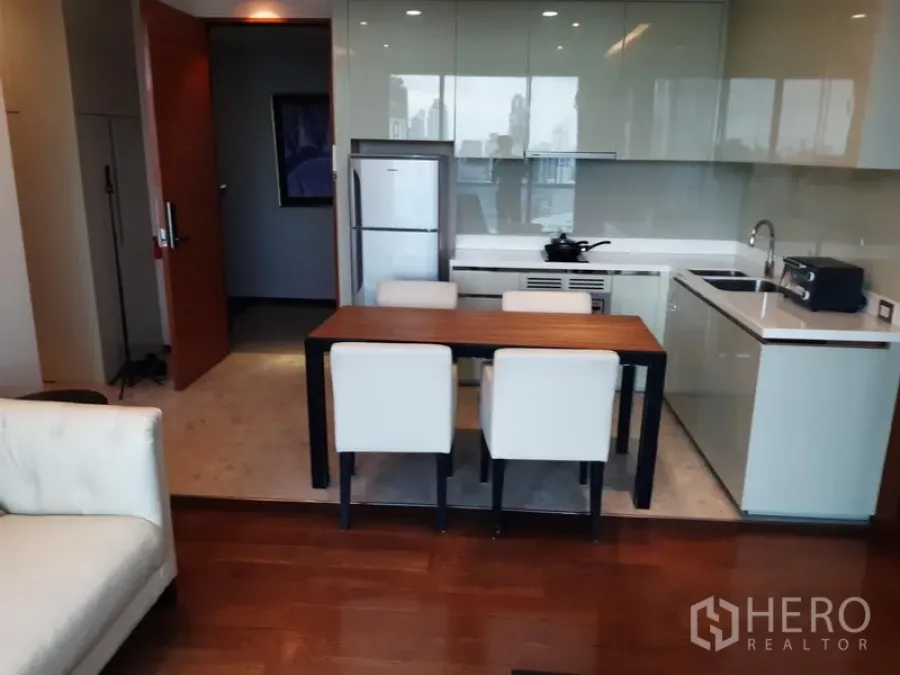 Condominium for rent or sale in Khlong Toei, Bangkok - Open-plan kitchen with glossy cabinets, refrigerator and dining table for four.