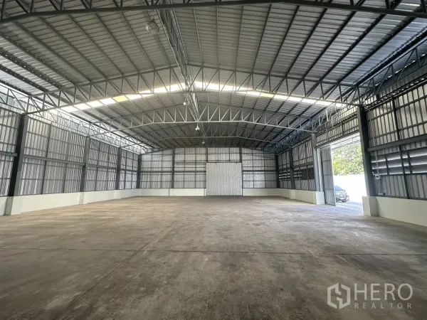 Warehouse for rent in Mueang Pathum Thani, Pathum Thani - Interior looking toward the entrance with large sliding doors, metal walls and high-bay lighting.