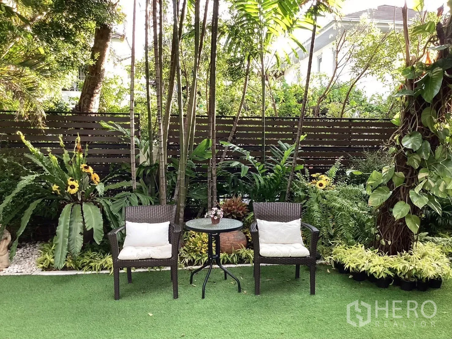 独栋房屋 for sale in Suan Luang, Bangkok - 遮荫热带花园，草坪上摆放两把藤椅和一张圆桌。