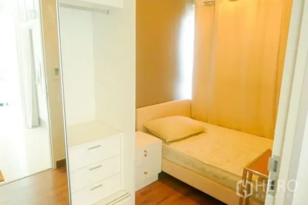 Condominium for rent or sale in Khlong San, Bangkok - Cozy secondary bedroom with single bed, white wardrobe, wood flooring and beige curtains.