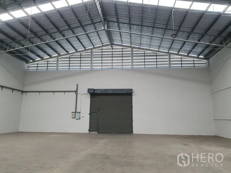 货栈 出租在Khlong Luang, Pathum Thani - 仓库内配有大卷闸门、通风百叶与白色墙面。