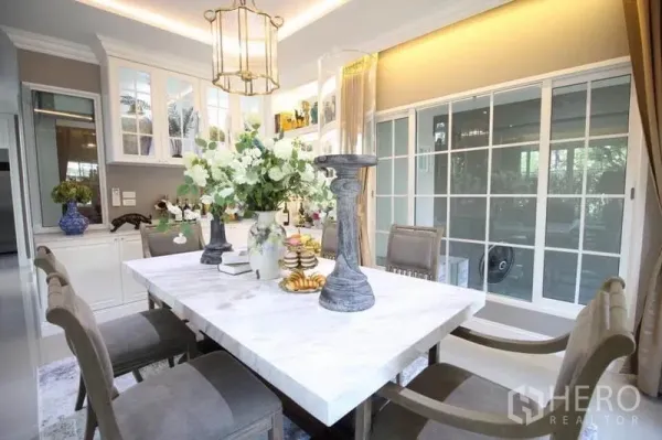 Detached House for rent or sale in Lat Phrao, Bangkok - Close-up of dining area with white marble table, high-back chairs and floor-to-ceiling sliding windows.