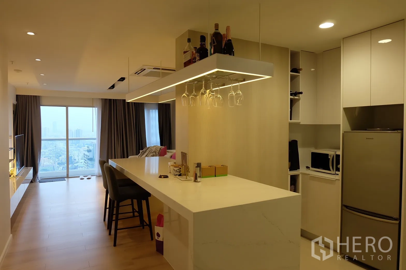Condominium for rent in Bang Rak, Bangkok - Open-plan kitchen with long quartz island, hanging wine-glass rack and city-view living area.