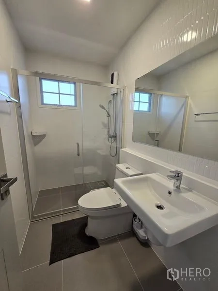 Detached House for rent in Bang Phli, Samut Prakan - Modern bathroom featuring a glass shower enclosure, large mirror, white sink and toilet.