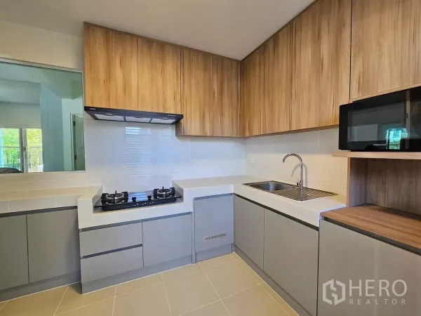 Detached House for rent in Bang Phli, Samut Prakan - Fitted L-shaped kitchen with gas hob, hood, microwave and ample cabinetry.