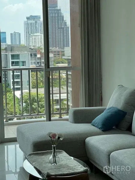 公寓 出售在Watthana, Bangkok - 客厅灰色转角沙发，落地窗通往阳台，远眺曼谷城市景观