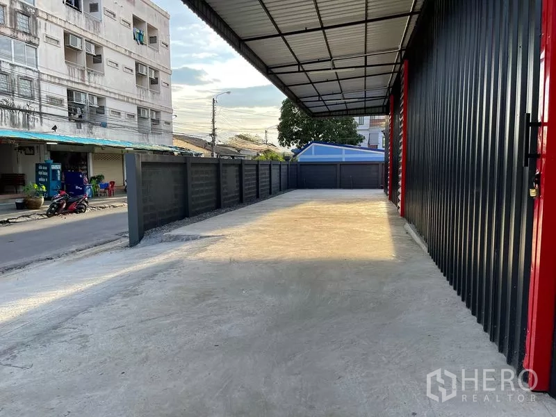 Warehouse for rent in Bang Kapi, Bangkok - Wide covered loading area with concrete floor along the fence and warehouse facade, offering ample truck space.