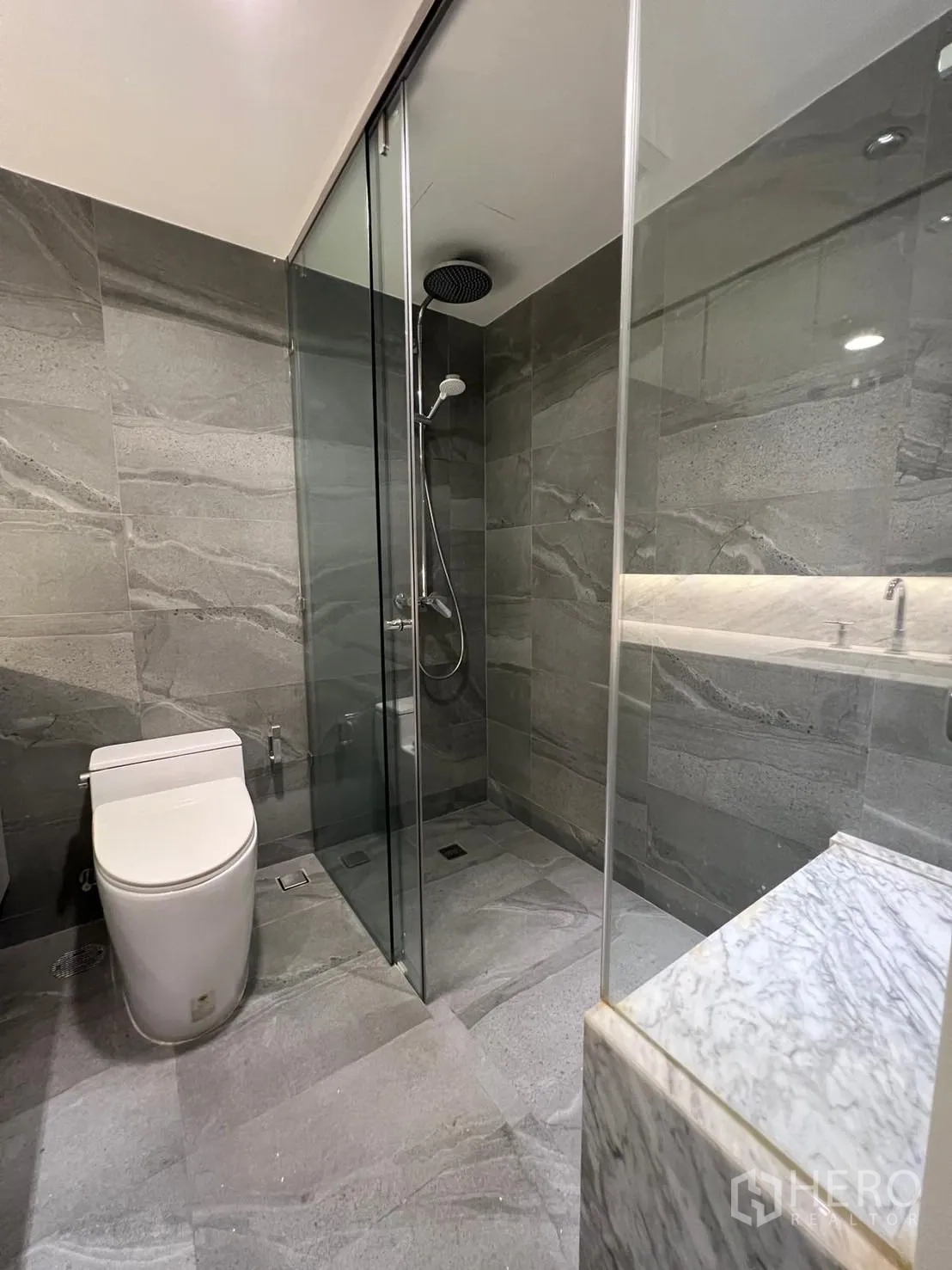 Condominium for rent or sale in Sathon, Bangkok - Sleek gray-tiled bathroom with glass-enclosed rain shower and toilet.