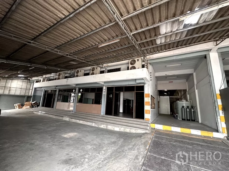 Factory for rent in Bang Phli, Samut Prakan - Covered loading zone with ramp access and a glass-fronted office block beneath a mezzanine.