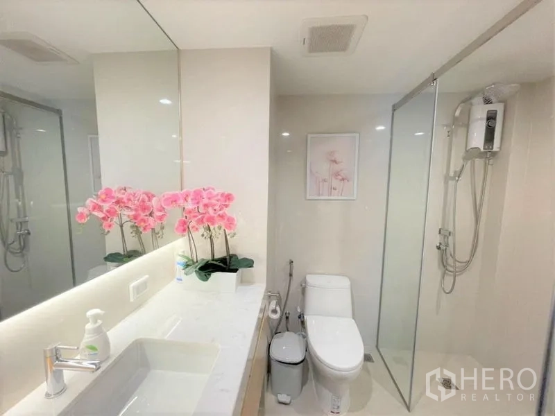 Condominium for rent or sale - Clean bathroom with glass-enclosed shower, long vanity, large mirror and orchid decor.