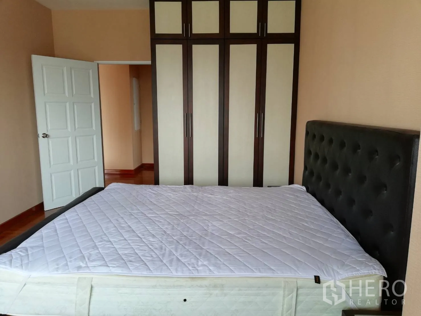 Condominium for rent in Watthana, Bangkok - Bedroom with padded headboard, tall wardrobe storage and white paneled door providing ample space.