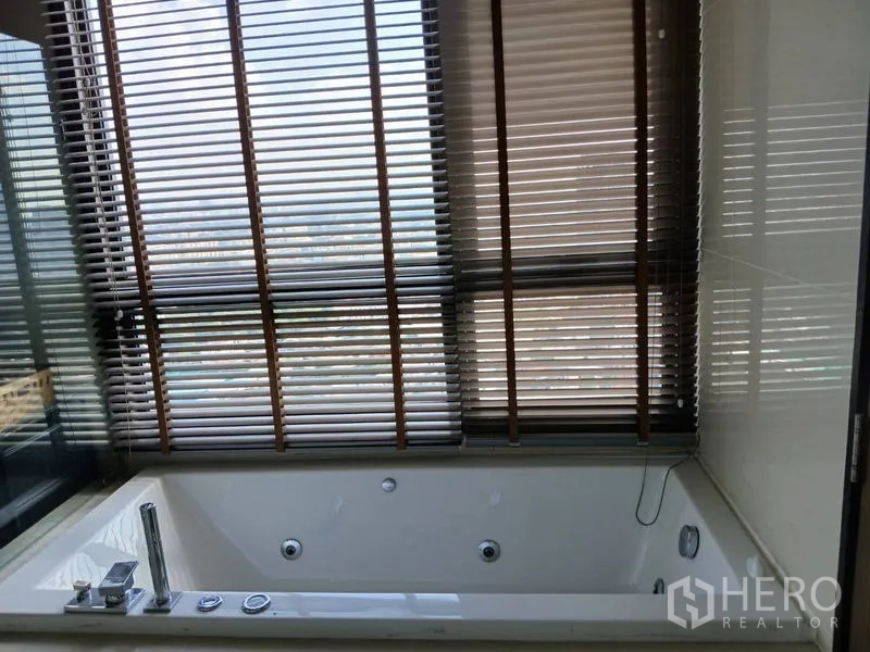 Condominium for rent - Bathroom with window-side soaking tub and blinds framing a city outlook.