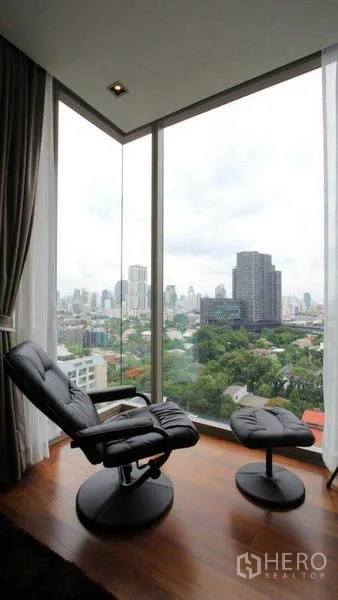 Condominium for rent - Corner reading nook with black recliner next to tall windows and skyline panorama.
