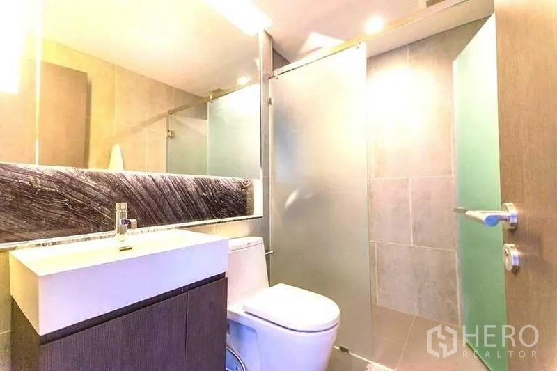 Condominium for rent in Khlong Toei, Bangkok - Contemporary bathroom with vanity, toilet and a frosted-glass shower enclosure.