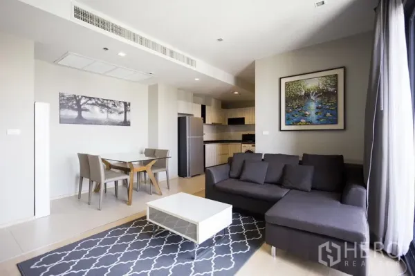 Condominium for rent in Watthana, Bangkok - Living area featuring a gray sectional, dining table and modern kitchen with stainless refrigerator and cabinets.