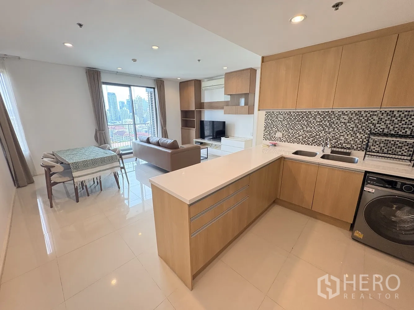 คอนโด for rent in Ratchathewi, Bangkok - พื้นที่นั่งเล่นและรับประทานอาหารแบบเปิดโล่ง พร้อมครัวรูปตัวแอล ผนังโมเสก เครื่องซักผ้า โซฟา โต๊ะกินข้าว และวิวเมืองผ่านกระจกบานใหญ่