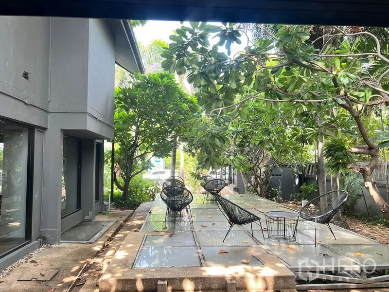 Retail Space for rent in Bangkok - Garden patio seating beside a gray building and mature tropical trees.