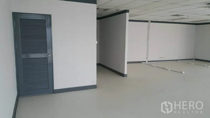 Office Space for rent in Khlong Toei, Bangkok - Interior corner with grey louvered door, partition walls, and clean white flooring.