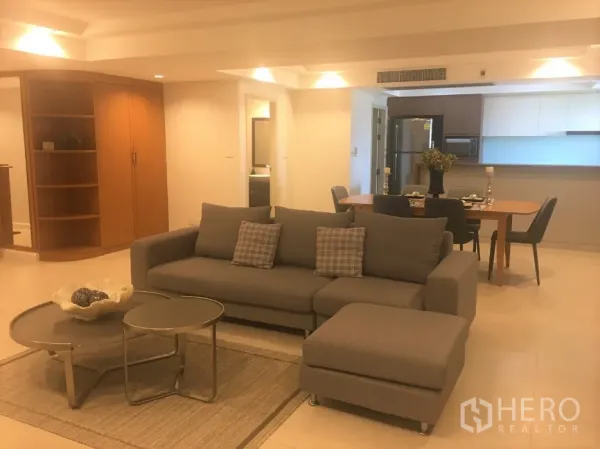 公寓 出租在Watthana, Bangkok - 开放式客厅，灰色沙发、巢式茶几，旁连餐区与现代化厨房。