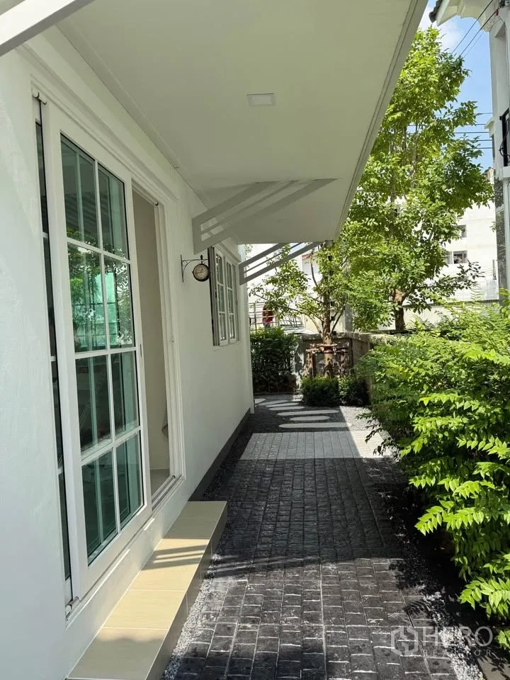Semi-detached House for rent in Mueang Samut Prakan, Samut Prakan - Side patio with sliding glass door, awnings, and landscaped hedges.