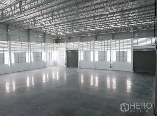 Factory for rent in Bang Sao Thong, Samut Prakan - Spacious warehouse interior with an 8 m high steel truss roof, polished concrete floor and multiple roller shutter entrances.