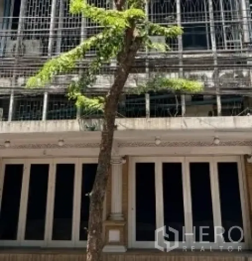 Shophouse for rent in Bang Rak, Bangkok - Street-facing shophouse facade with tall windows, metal grilles and a slim tree in Bang Rak.