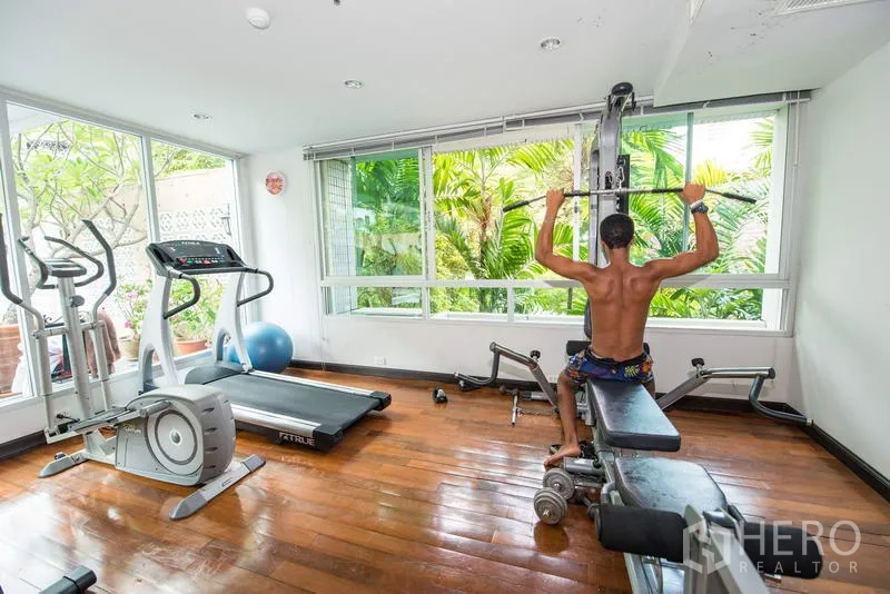 Apartment for rent in Sathon, Bangkok - Fitness room with cardio machines and weight station facing garden windows.