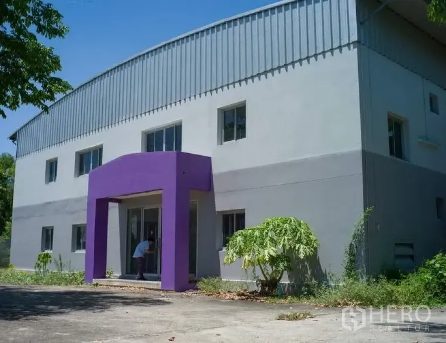 Factory for rent in Pathum Thani - Modern factory facade with purple entrance canopy and glass doors in a landscaped yard.