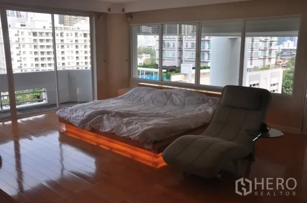 Condominium for rent in Khlong Toei, Bangkok - Spacious master bedroom with platform bed underlighting, chaise lounge, hardwood floors and panoramic city views.