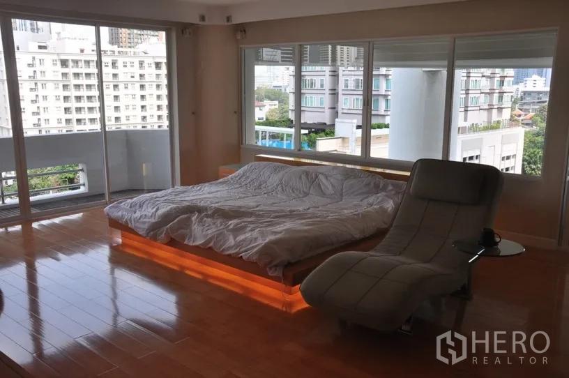 Condominium for rent in Khlong Toei, Bangkok - Spacious master bedroom with platform bed underlighting, chaise lounge, hardwood floors and panoramic city views.