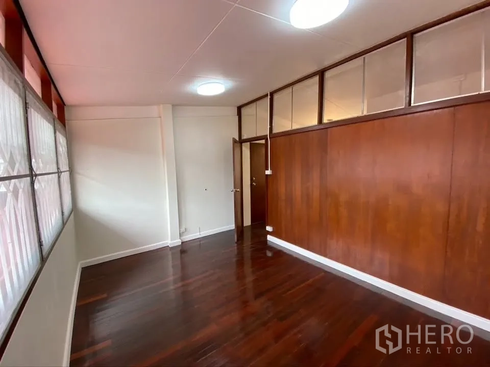 Detached House for rent in Suan Luang, Bangkok - Long room with wood panel wall, polished floors, and grilled windows.