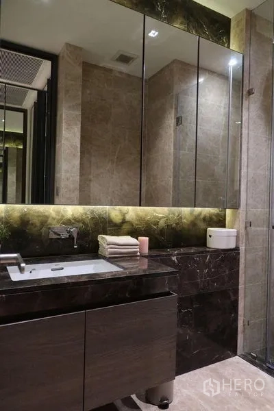 Condominium for rent in Pathum Wan, Bangkok - Luxurious bathroom with marble walls, large mirrored cabinet, vanity and glass shower.