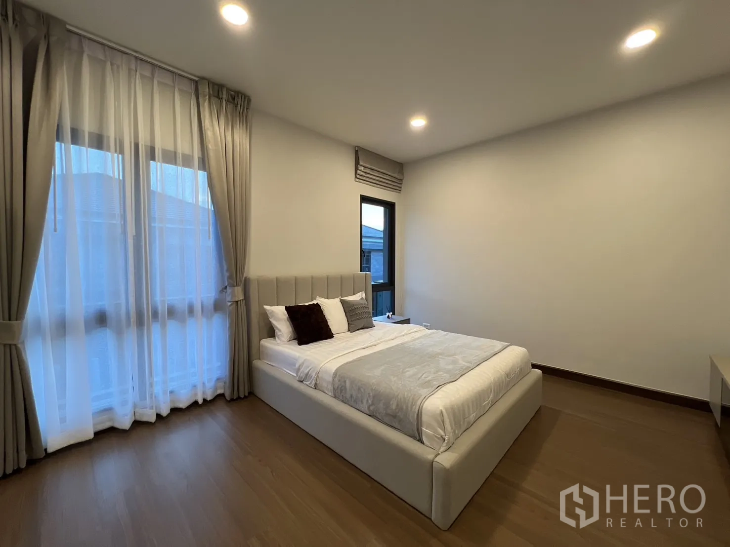Detached House for rent in Bang Phli, Samut Prakan - Third bedroom with grey upholstered bed and floor-to-ceiling curtains.