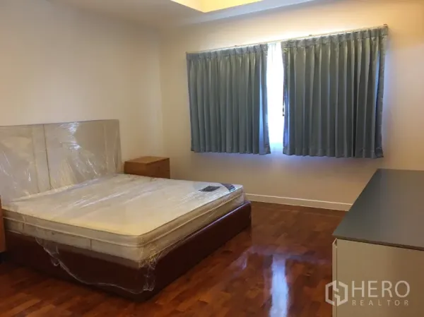 บ้าน ให้เช่าในWatthana, Bangkok - ห้องนอนรองพื้นไม้ หน้าต่างคู่ผ้าม่านสีน้ำเงิน พร้อมโต๊ะหัวเตียง.