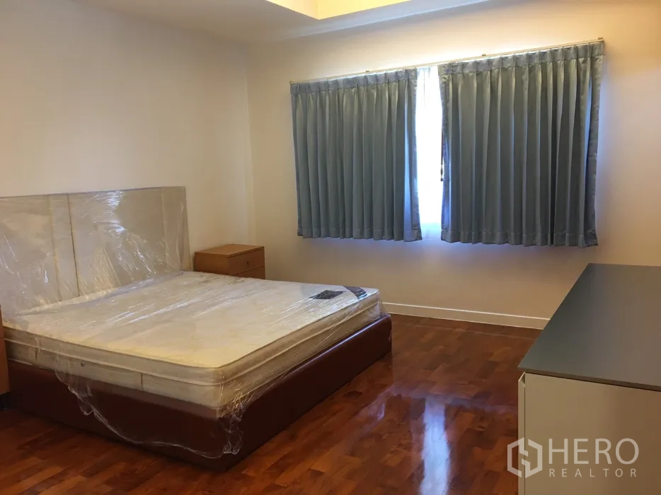 บ้าน ให้เช่าในWatthana, Bangkok - ห้องนอนรองพื้นไม้ หน้าต่างคู่ผ้าม่านสีน้ำเงิน พร้อมโต๊ะหัวเตียง.