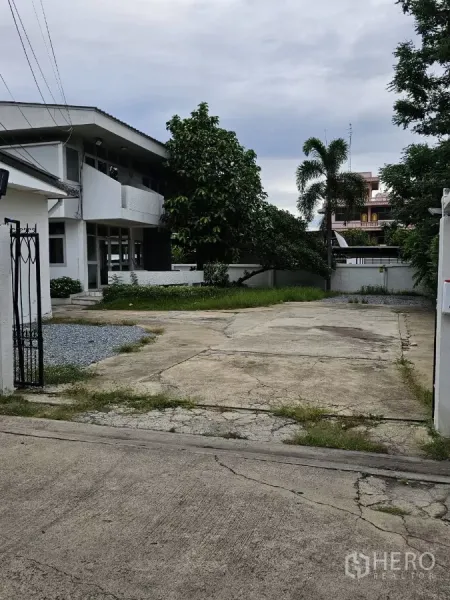 บ้าน ให้เช่าหรือขายในLat Phrao, Bangkok - ประตูรั้วและทางเข้าคอนกรีตกว้างสู่บ้านเดี่ยวสองชั้นสีขาวพร้อมสวน