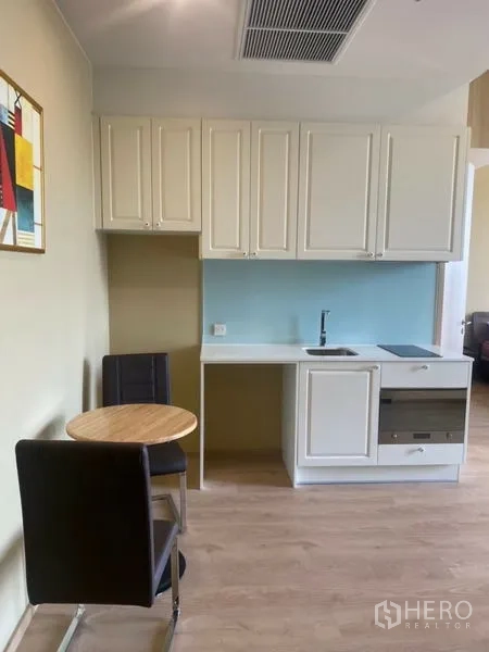 Condominium for rent in Watthana, Bangkok - Compact kitchenette with white cabinetry, cooktop, built-in oven and dining table for two.